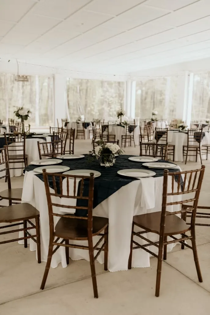 Wedding reception tables with white linens, dark runners and floral centrepieces