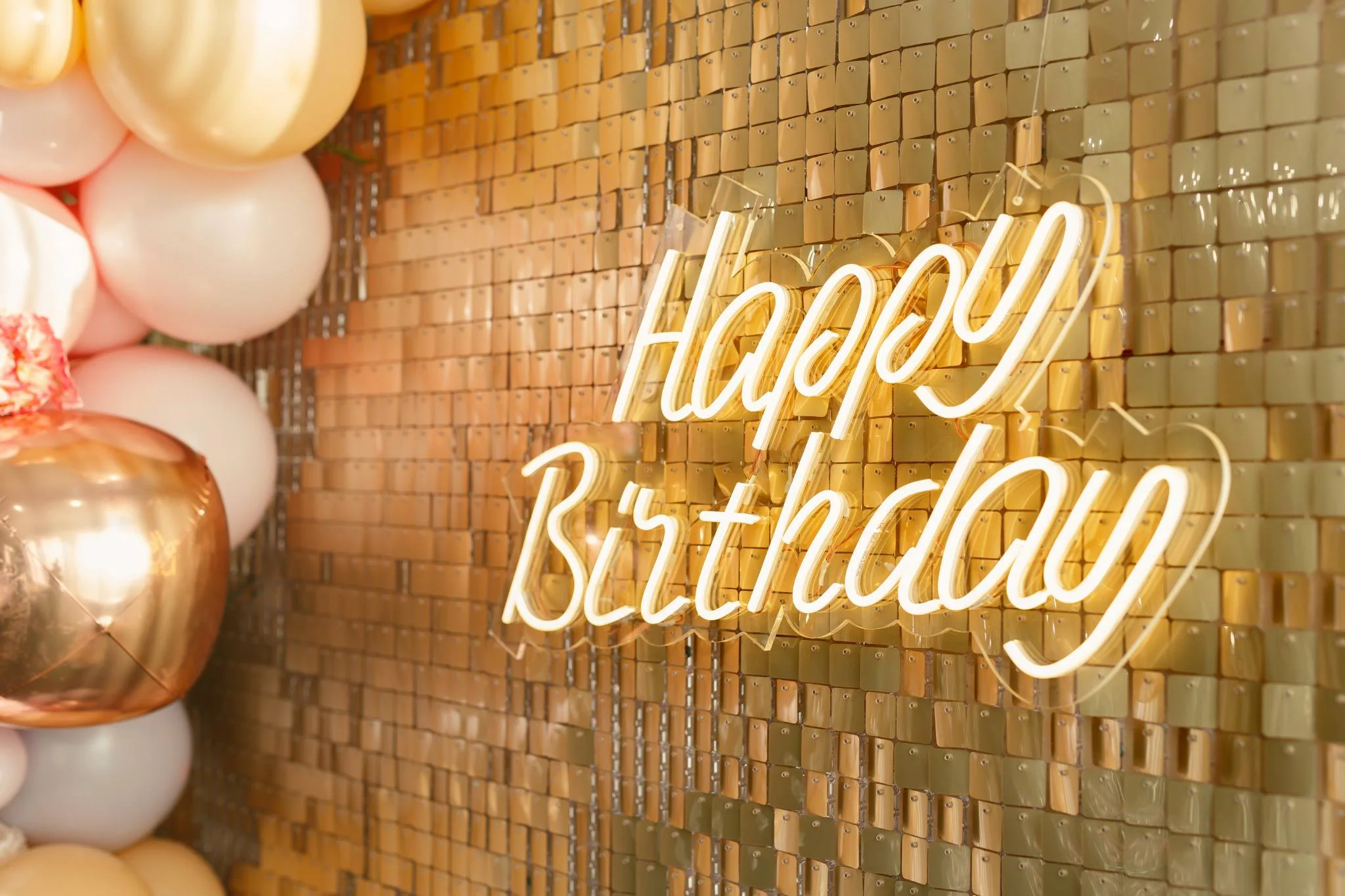An illuminated Happy Birthday neon sign against a gold event backdrop